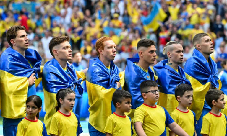 Jugadores ucranianos se arropan con la bandera de su país a su salida al campo